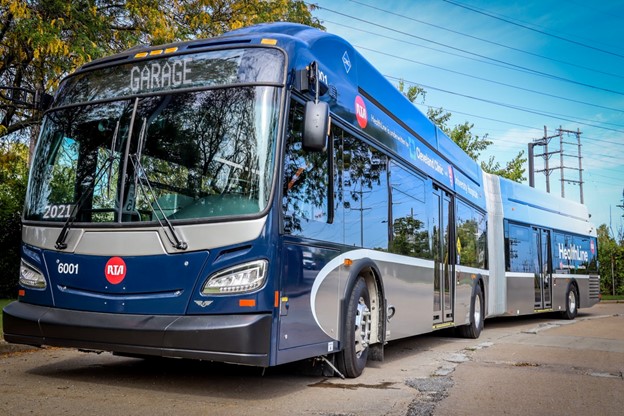 Blue bus stationed at a bus stop with trees behind it. 