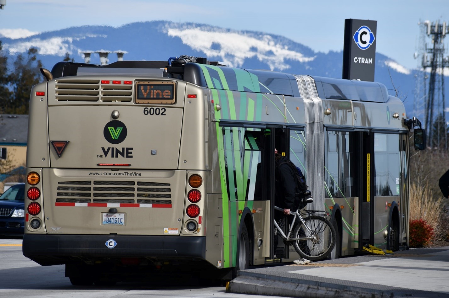 Vine bus parked at the c-tran station while a passenger steps on the bus with his bike. There are mountains in the background of the bus.